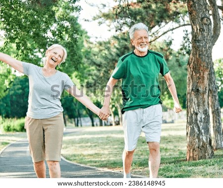Smiling active senior couple jogging exercising and having fun and celebrating success rasing hands together taking a break in the park Royalty-Free Stock Photo #2386148945
