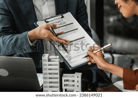 An Asian salesman offers to sell a house to an African customer. An Asian man, a real estate agent, shakes hands with a female African American client while purchasing an apartment.