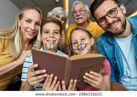 Portrait of a three generation famili, grandparents, parents and children sitting on sofa and having fun reading a book at home Royalty-Free Stock Photo #2386152653