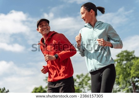 Young Asian couple are exercising with outdoor running with a park background in the morning. Concept healthy running and outdoor exercise,Tracking shot.