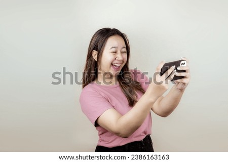 Portrait of a happy young Asian woman playing a game on a smartphone, isolated on a plain background