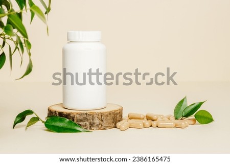 Supplement white bottle with herbal pills on wooden podium. Vitamins  bottle mockup with pills and green leaves on beige background, organic medication. Natural herbal vitamins, healthy lifestyle. Royalty-Free Stock Photo #2386165475