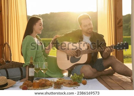 Romantic date. Beautiful woman listening to her boyfriend playing guitar during picnic outdoors