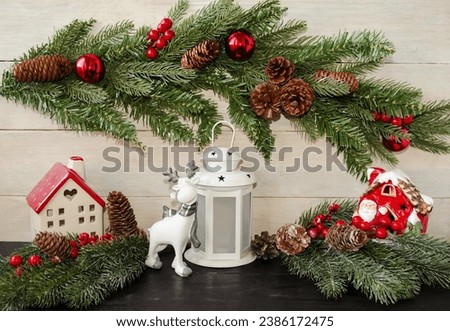 Christmas card, on a light wooden background, New Year's decorated fir branches, a cute deer and a white lantern, Santa Claus's house.  Background image front view.  New Year and Christmas holiday.