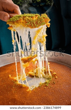 A tray of Syrian Nabulsiyeh dessert with someone taking a piece of it and spreading the cheese Royalty-Free Stock Photo #2386174899