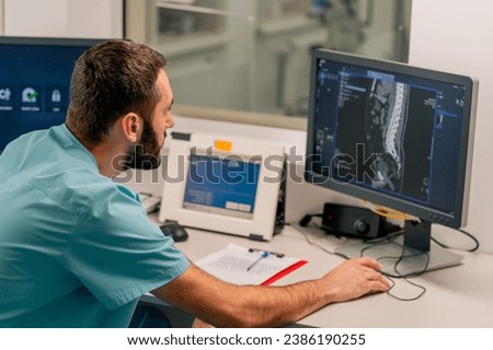 Concentrated male physician sits at a computer monitor in a room for a describing MRI images and monitoring patient's condition
