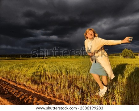 An adult girl in a field and with a stormy sky with clouds posing for picture in the rain. A woman having fun outdoors on rural and rustic nature