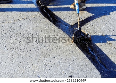During worker patcher performs coated filling asphalt cracks sealing bitumen emulsion road surface restoration work Royalty-Free Stock Photo #2386210449