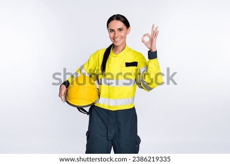 Photo of cheerful good mood young firewoman dressed yellow uniform helmet showing okey isolated white color background