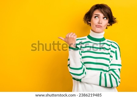 Photo of doubtful suspicious lady wear striped pullover pointing thumb looking empty space isolated yellow color background
