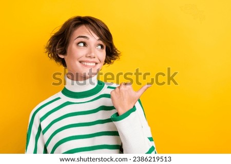 Photo of excited cheerful girl dressed striped sweater looking showing thumb empty space isolated yellow color background