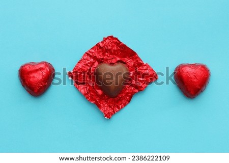 Three red heart-shaped candies on a blue paper background, top view.Two chocolates and one with an unwrapped wrapper.