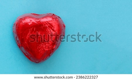 Large heart-shaped candy in red foil on a blue paper background. Flat lay.
