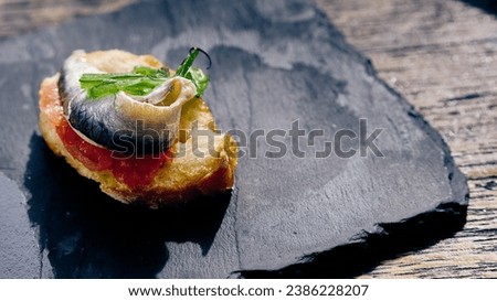 Savor the taste of gourmet sophistication with this exquisite canapé, featuring a silvery slice of anchovy elegantly perched atop a fresh bed of tomato on a crispy crostini.  Royalty-Free Stock Photo #2386228207