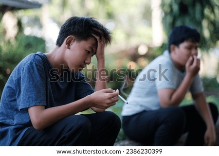 Teenagers underage smoking a cigarette causes bad habits causing addiction. Asian kid smoking behind the school, feeling sad, unhappy, stressed in an old dirty grungy place. Royalty-Free Stock Photo #2386230399