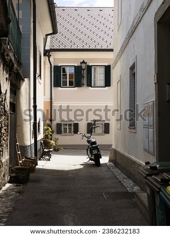 A narrow quiet street in an old small town. Little signs of life in the street - a bench, flowers, a parked motorbike, a dustbin... Radovljica, Slovenia, Europe Royalty-Free Stock Photo #2386232183
