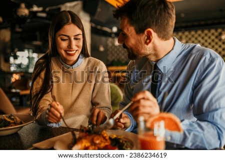 Two diverse colleagues enjoying a casual business lunch at a vibrant restaurant, sharing a moment of camaraderie over a delicious meal Royalty-Free Stock Photo #2386234619