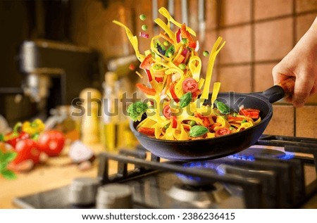Preparing Italian pasta with vegetables in a frying pan on the gas stove for evening dinner at home kitchen Royalty-Free Stock Photo #2386236415