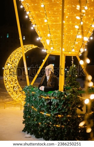 Beautiful woman in warm clothes, a hat and a coat in winter against the background of Christmas street lights. Celebrates the New Year on the street against the backdrop of street decor. bokeh