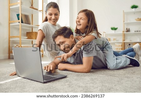 Portrait of a joyful happy young family with child girl lying on the floor in the living room at home using laptop. Smiling parents watching funny cartoon online or talking on video call.