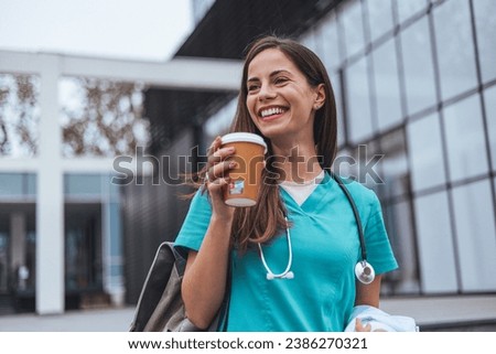 The young adult female nurse drinks her coffee as she arrives to work at the hospital. A young adult female nurse arrives for a shift in a hospital. She is wearing medical scrubs