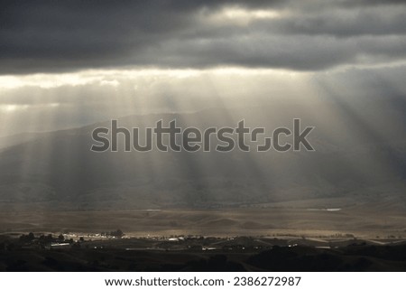 sunrays shinning through the cloud onto a small valley Royalty-Free Stock Photo #2386272987