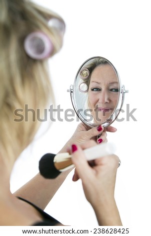Middle aged woman smiling while looking at mirror against a white background