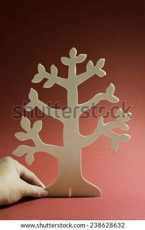 Hand holding a standing wooden tree with branches and no tree for room of text on a red background.