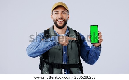 Happy man, backpack and pointing to phone green screen on mockup or hiking app against a studio background. Portrait of male person or hiker smile and showing mobile smartphone display or travel tips Royalty-Free Stock Photo #2386288239