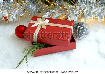 Christmas composition with fir tree branches, red gift box and silver tinsel in golden light of garland