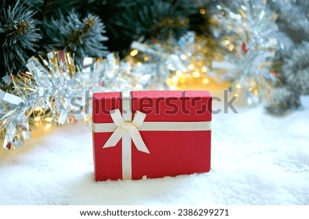 Christmas composition with fir tree branches, red gift box and silver tinsel in golden light of garland