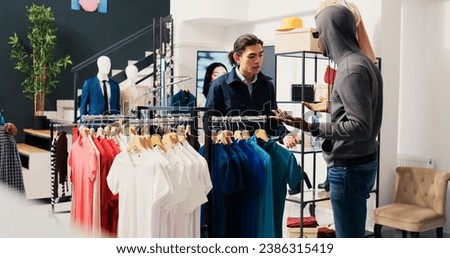 Robber trying to stole stylish clothes from shopping mall, being caught by asian security guard. African american couple arguing with bodygurad, trying to escape crime accusation in modern boutique Royalty-Free Stock Photo #2386315419