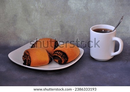 A plate with three fresh poppy seed buns and a cup of hot black coffee on a gray background. Close-up.