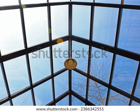 A lamp hanging on glass roof with blue sky background.