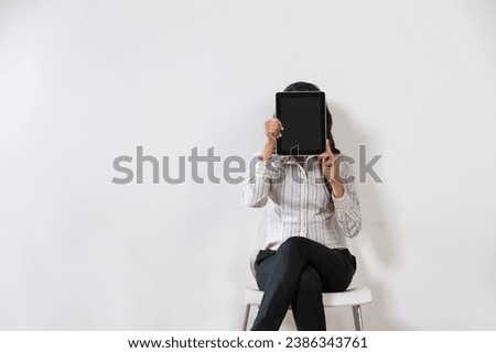 Indian business woman covering her face with a digital tablet.