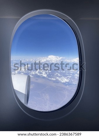 Blue sky and clouds seen through an airplane window, airplane window view Royalty-Free Stock Photo #2386367589