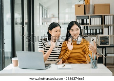 Two Attractive young Asian female college students working on the school project using laptop computer and tablet together, enjoy talking and snacking 