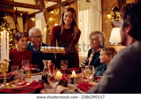 Happy woman serving Christmas pie to her extended family at dining table.