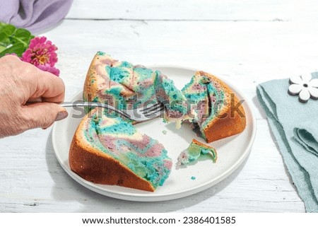 Apple pie in unicorn colors ready to eat. Female hands hold cutlery, homemade baking, nostalgic food. Hard light, dark shadow, white wooden background, copy space
