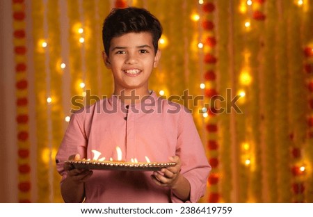 Happy Indian Kid boy Celebrating diwali holding plate full of diyas