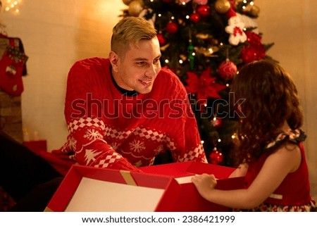 young man opening a gift box with a little girl on Christmas day at home