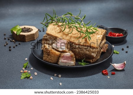 Pieces of salty high-fat meat cooked with spices. Salo, bacon, lard, silverside, gammon. Garlic, fresh bay leaves, rosemary, spices, chili. Black stone concrete background, copy space