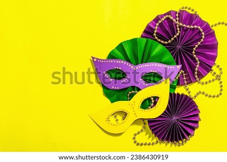 Festive Mardi Gras masquerade yellow background. Fat Tuesday carnival, masks, beads, traditional decor. Symbolic colors, trendy hard light, dark shadow, flat lay, top view