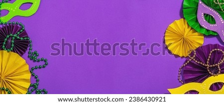 Festive Mardi Gras masquerade purple background. Fat Tuesday carnival, masks, beads, traditional decor. Symbolic colors, trendy hard light, dark shadow, flat lay, banner format Royalty-Free Stock Photo #2386430921