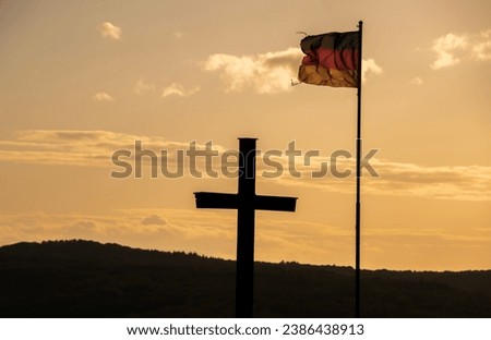 photo of cross and german flag against the sky at sunset