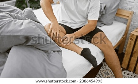 Awake early in the morning, a young chinese man suffers from agonizing leg pain in his home bedroom, anxiously massaging his injured limb Royalty-Free Stock Photo #2386454993