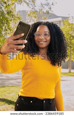 Vertical portrait African American woman smiling taking a photo of herself with a smartphone outdoors.