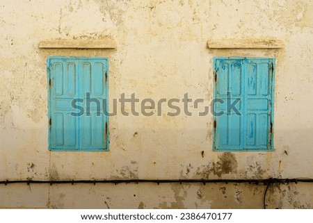 View of blue windows and shutters on an old house wall with pilling white paint. Essaouira (Mogador), Morocco Royalty-Free Stock Photo #2386470177
