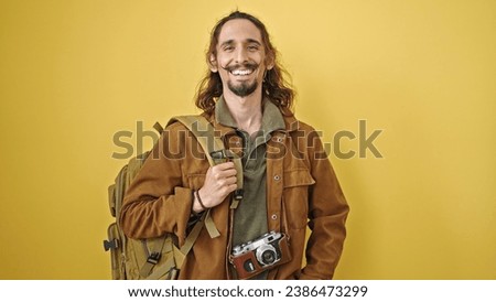 Young hispanic man tourist wearing backpack smiling over isolated yellow background