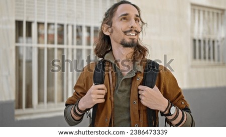 Young hispanic man tourist wearing backpack smiling at street